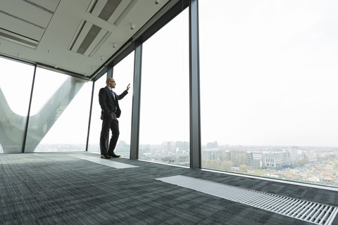 Geschäftsmann auf leerer Büroetage schaut aus dem Fenster, lizenzfreies Stockfoto