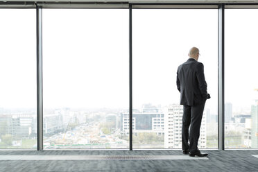 Businessman on empty office floor looking out of window - WESTF019473