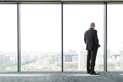 Businessman on empty office floor looking out of window - WESTF019473