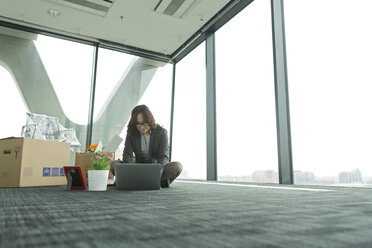 Businesswoman using laptop on empty office floor with cardboard boxes - WESTF019314