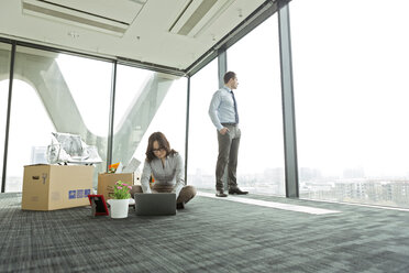 Businesswoman using laptop on empty office floor with cardboard boxes - WESTF019485