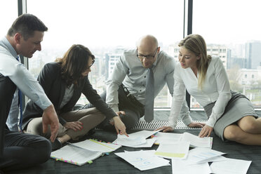 Businesspeople sitting on floor discussing papers - WESTF019319