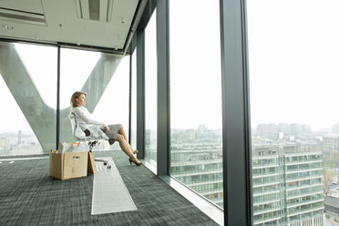 Geschäftsfrau auf leerer Büroetage mit Pappkarton und Blick aus dem Fenster - WESTF019491