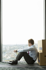 Geschäftsmann lehnt an Kartons und schaut aus dem Fenster - WESTF019502