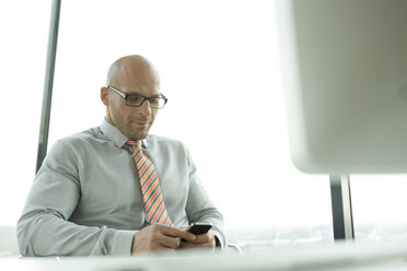 Businessman at desk looking at cell phone - WESTF019292