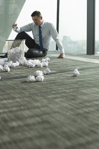 Geschäftsmann sitzt auf dem Büroboden, umgeben von zerknittertem Papier, lizenzfreies Stockfoto