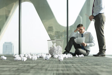 Zwei Geschäftsleute auf dem Boden eines Büros, umgeben von zerknittertem Papier - WESTF019301