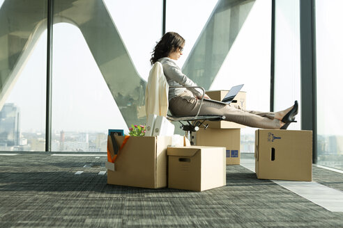 Businesswoman using laptop with feet on cardboard boxes - WESTF019303