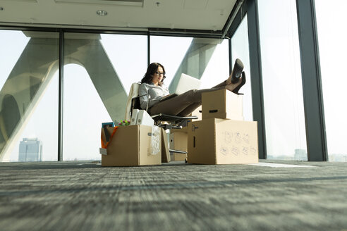 Businesswoman using laptop with feet on cardboard boxes - WESTF019305