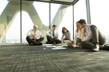 Businesspeople sitting on floor discussing papers - WESTF019385