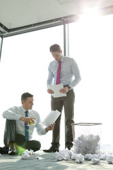 Zwei Geschäftsleute auf dem Boden eines Büros, umgeben von zerknittertem Papier - WESTF019409