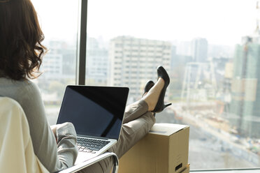 Businesswoman using laptop with feet on cardboard boxes - WESTF019411