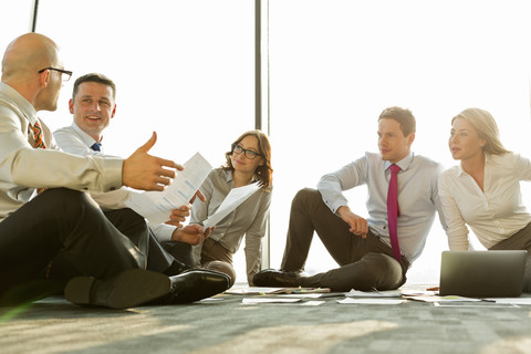 Geschäftsleute sitzen auf dem Boden und besprechen Papiere, lizenzfreies Stockfoto