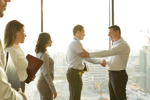 Two businessmen in sunny office shaking hands - WESTF019525