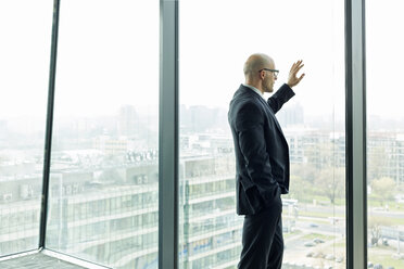 Nachdenklicher Geschäftsmann auf der Büroetage mit Blick aus dem Fenster - WESTF019354