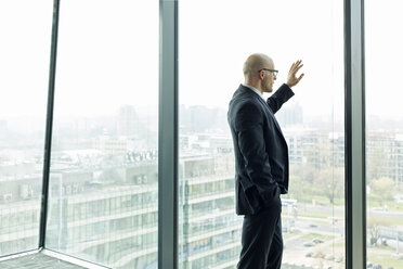 Thoughtful businessman on office floor looking out of window - WESTF019354