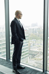 Nachdenklicher Geschäftsmann auf der Büroetage mit Blick aus dem Fenster - WESTF019355
