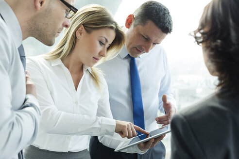 Businesspeople in office with woman using digital tablet - WEST019435