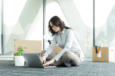 Geschäftsfrau mit Laptop auf leerem Büroboden mit Kartons - WESTF019365