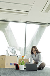 Glückliche Geschäftsfrau mit Laptop auf leerem Büroboden mit Kartons - WESTF019529
