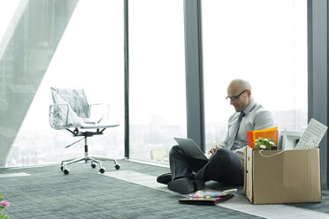 Geschäftsmann mit Laptop auf leerem Büroboden mit Pappkarton - WESTF019366