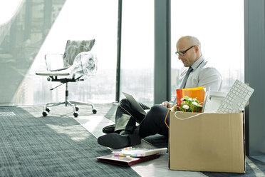 Geschäftsmann mit Laptop auf leerem Büroboden mit Pappkarton - WESTF019367