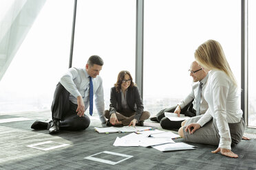 Businesspeople sitting on floor discussing papers - WEST019530