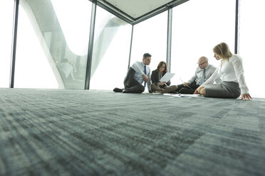 Businesspeople sitting on floor discussing papers - WEST019441