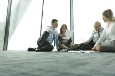 Businesspeople sitting on floor discussing papers - WEST019442