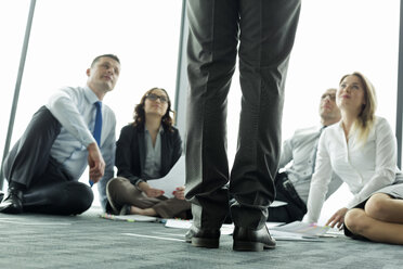 Geschäftsleute, die auf dem Boden sitzen und zu einem Kollegen aufschauen - WEST019443