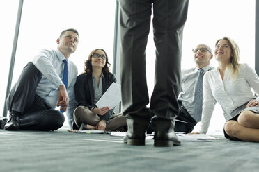 Geschäftsleute, die auf dem Boden sitzen und zu einem Kollegen aufschauen - WEST019444