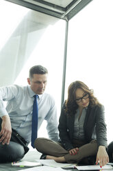 Businesspeople sitting on floor discussing papers - WEST019446