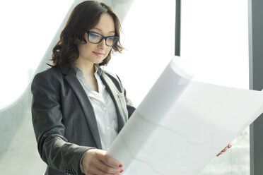 Businesswoman in office looking at blueprint - WESTF019452