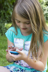 Kleines Mädchen sitzt mit Smartphone im Garten - YFF000164