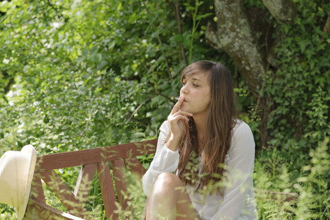 Young woman smoking on wooden bench in a garden stock photo