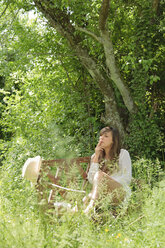 Junge Frau raucht auf einer Holzbank in einem Garten - LAF000896