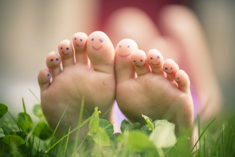 Kleine Mädchenfüße mit bemalten Zehen im Gras liegend, lizenzfreies Stockfoto