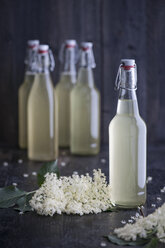 Glasflaschen mit hausgemachtem Holunderblütensirup und Holunderblüten auf dunklem Holz - IPF000121