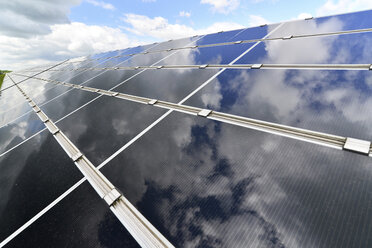 Germany, photoelectric cells of solar power plant with reflections of clouds, partial view - LYF000061