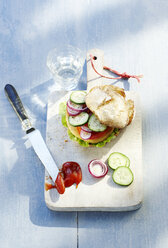 Chicken burger, cucumber, onion and ketchup on chopping board - KSWF001310