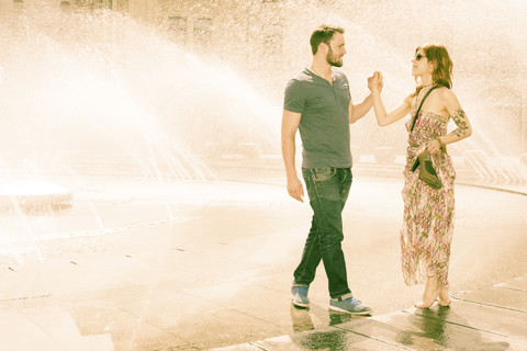 Deutschland, Bayern, München, junges verliebtes Paar steht Hand in Hand vor einem Brunnen am Stachus, lizenzfreies Stockfoto