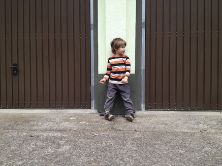 Kind steht auf Füßen kippelnd zwischen zwei Garagentoren. Berlin, Deutschland - ZMF000302