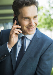Porträt eines lächelnden Geschäftsmannes, der mit einem Smartphone telefoniert - UUF000870