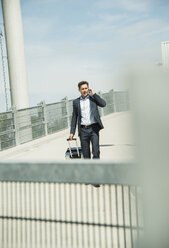 Business man with rolling suitcase telephoning with smartphone - UUF000878