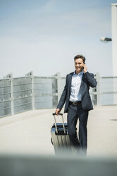 Business man with rolling suitcase telephoning with smartphone - UUF000879