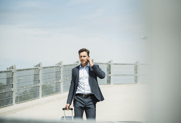 Business man with rolling suitcase telephoning with smartphone - UUF000880
