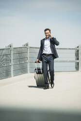 Business man with rolling suitcase telephoning with smartphone - UUF000881