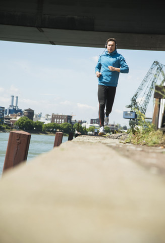 Man with headphones jogging at riverside stock photo