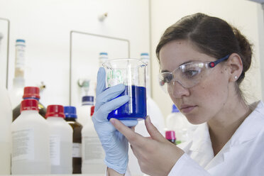 Portrait of young female chemist holding Beaker with blue liquid - SGF000765