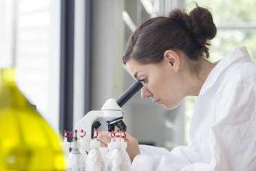 Portrait of young female chemist looking through microscope - SGF000769